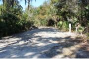 Looking into site from campground road; water spigot and electrical hook up on right; picnic table and fire ring on left; site mixture of grass and sand