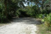 Looking into site from campground road; water spigot and electrical hook up on right; picnic table and fire ring on left; site mixture of grass and sand