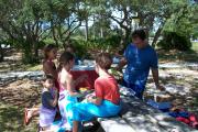 A family in brightly colored clothing enjoying a snack in the shade on a picnic table at Big Lagoon State Park.