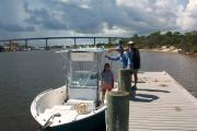 Three adults in the bright sunshine preparing to board a boat at Big Lagoon State Parkâs boat launch on the still waters of the Intracoastal Waterway.