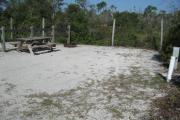View of a picnic table, fire ring and fence in bright sunshine.