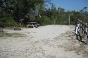 View of a picnic table, fire ring and fence in bright sunshine.