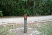 Close up of a brown campsite marker on a wooden post with mowed grass in the foreground and thick bushes to the side and background. This site is a back in site and will accommodate a 56 foot camper.