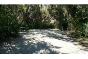 This is a view of campsite 7 from the circle drive looking in. You can see the picnic table and fire ring/grill to the left and the utility hookups to the right, which includes electricity and water spigots. The site is surrounded with medium size trees, including oak, hickory and pine along with palmetto bushes.