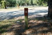 Close up of a brown campsite marker on a wooden post indicating campsite number 14, with a mostly open view. This site is a beautiful 48 foot back in site and is partially shaded. This site is across the entrance road and in site of the new playground.