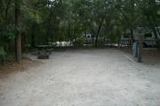 This is a picture of campsite16 looking into the campsite from the road. On the left of the picture one can see a wooden picnic table and a ground fire ring/grill. On the right of the picture one can see the electric and water hook up. The site is surrounded by a scattering of oaks and a few Florida pines.