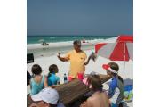 A volunteer staff member delivers an interpretive program on sea life to a group of park visitors on the sand with the Gulf of Mexico as the backdrop at Henderson Beach State Park.