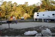 This photo shows an empty site with three large rocks near the gravel pad and with only grass around the site. Other camping set ups are visible along a short distance to the bathhouse.