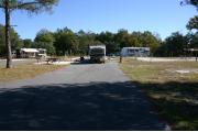 This photo shows an empty paved ADA accessible site with 2 trees near and only grass surrounding the site. Another RV is visible. This site is a short distance to the bathhouse