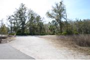 Photo shows a pull through gravel site with trees on one side. The photo shows a camperâs RV with the awnings out.