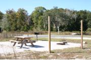 This photo shows the empty gravel pad. There is only grass surrounding this site with one tree near by.