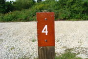 Photo: 004, View of site number post white on brown, bushes visible in the back ground.