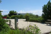 Photo: 010, View of gravel campsite with picnic table and grill, RV and bushes in background.