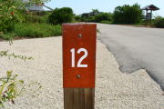 Photo: 012, View of site number post white on brown, bushes visible in the back ground.