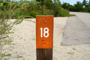 Photo: 018, View of site number post white on brown, bushes visible in the back ground.
