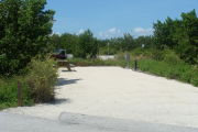 Photo: 018, View of gravel campsite with picnic table and grill, Atlantic Ocean and bushes in background.