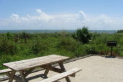 Photo: 019, View of gravel campsite with picnic table and grill, Atlantic Ocean and bushes in background.