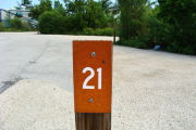 Photo: 021, View of site number post white on brown, bushes visible in the background.