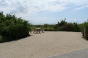 Photo: 022, View of gravel campsite with picnic table and grill, Atlantic Ocean and bushes in background.
