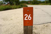 Photo: 026, View of site number post white on brown, bushes visible in the background.