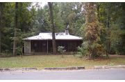From this view you see that the cabin is set back off the service road a little further that the other cabins. As with the other cabins it is nestled on three sides by hardwood hammock. An L shaped screened porch runs across most of the front of the cabin and then turns and runs to the end of the side of the cabin. On the porch are two rocking chairs, a porch swing and a picnic table. There are two doors leading into the cabin proper. One is to the front of the cabin and the other one is to the kitchen, near the back of the cabin. There is rear screen door that leads to the back outside area of the cabin.