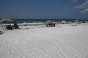 Visitors to Topsail Hill State Park enjoying the white sand beach, lounging under beach umbrellas, and wading in the Gulf of Mexico.