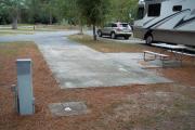 A view of RV site four at Topsail Hill Preserve State Park looking towards the front of the site.  A picnic table is on a concrete pad to the right of the site and utility hook up boxes are to the left.