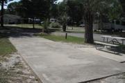 A view of RV site six at Topsail Hill Preserve State Park looking towards the front of the site.  A picnic table is on a concrete pad to the right of the site.  The bathhouse is visible in the background of the picture.