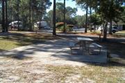 A view of RV site seven at Topsail Hill Preserve State Park looking towards the front of the site.  A picnic table is on a concrete pad to the right of the site.  The bathhouse and other RV sites are visible in the background.