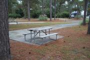 A view of RV site nine at Topsail Hill Preserve State Park looking across the site.  A picnic table is on a concrete pad next to the site and other RV sites are visible in the background.