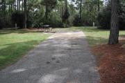 A view of RV site ten at Topsail Hill Preserve State Park looking towards the back of the site.  A picnic table is on a concrete pad to the left of the site and utility hook up boxes are to the right.