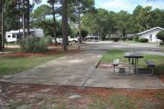 A view of RV site ten at Topsail Hill Preserve State Park looking towards the front of the site.  A picnic table is on a concrete pad to the right of the site.  The bathhouse and other RV sites are visible in the background.