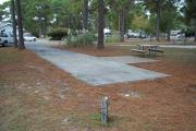 A view of RV site eleven at Topsail Hill Preserve State Park looking towards the front of the site.  A picnic table is next to a concrete pad to the right of the site.  The bathhouse is visible in the background.