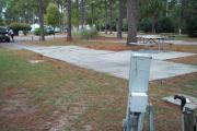 A view of RV site twelve at Topsail Hill Preserve State Park looking across the site.  A picnic table is on a concrete pad next to the site.  The utility hook up boxes are visible in the foreground.