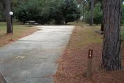 A view of RV site fourteen at Topsail Hill Preserve State Park showing the site marker, a picnic table to the left of the site, and utility hook up boxes to the right.  There is a small street lamp to the left of the site.