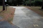 A view of RV site fourteen at Topsail Hill Preserve State Park looking towards the back of the site.  A picnic table is next to a concrete pad to the left of the site and utility hook up boxes are to the right of the site.  There is a small street lamp to the left of the site.