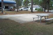 A view of RV site fourteen at Topsail Hill Preserve State Park looking across the site.  A picnic table is on a concrete pad next to the site.  The bathhouse is visible in the background.