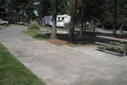 A view of RV site seventeen at Topsail Hill Preserve State Park looking across the site.  A picnic table is on a concrete pad next to the site with two pine trees growing next to it.  Other RV sites are visible in the background.