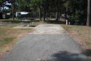 A view of RV site twenty at Topsail Hill Preserve State Park looking towards the back of the site.  A picnic table is on a concrete pad to the left of the site and utility hook up boxes are to the right of the site.  A small wooden bridge and other RV sites are visible in the background.
