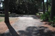 A view of RV site twenty-one at Topsail Hill Preserve State Park looking towards the back of the site.  A picnic table is on a concrete pad to the left of the site and utility hook up boxes are to the right of the site.
