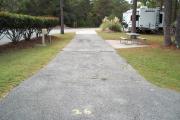 A view of RV site twenty-six at Topsail Hill Preserve State Park looking towards the back of the site showing that it is a pull through site open to the road at both ends.  A picnic table is on a concrete pad to the right of the site and the utility boxes are to the left.