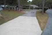 A view of RV site twenty-six at Topsail Hill Preserve State Park looking towards the front of the site showing that it is a pull through site open to the road at both ends.  A picnic table is on a concrete pad to the left of the site and the utility boxes are to the right.