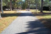 A view of RV site twenty-seven at Topsail Hill Preserve State Park looking towards the back of the site.  A picnic table is on a concrete pad to the left of the site and utility hook ups are to the right of the site.  A small wooden footbridge can be seen in the background.