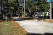 A view of RV site twenty-seven at Topsail Hill Preserve State Park looking towards the back of the site.  A picnic table is on a concrete pad to the right of the site and utility hook ups are to the left of the site.
