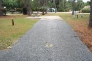 A view of RV site twenty-seven at Topsail Hill Preserve State Park looking towards the back of the site.  A picnic table is on a concrete pad to the left of the site and utility hook ups are to the right of the site.