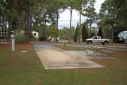 A view of RV site twenty-seven at Topsail Hill Preserve State Park looking towards the front of the site.  A picnic table is on a concrete pad to the right of the site and utility hook ups are to the left of the site.