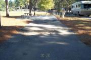 A view of RV site thirty-three at Topsail Hill Preserve State Park looking towards the back of the site.  A picnic table is on a concrete pad to the left of the site and utility hook up boxes are to the right of the site.  An RV is park in the site to the right.