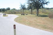 View of campsite #28 from site entry â This is a pull-through campsite, with an asphalt pad for camping units.  On the left of the asphalt pad is the electric hookup and water spigot, surrounded by a protective wooden enclosure.  On the right are a picnic table and a circular ground grill.