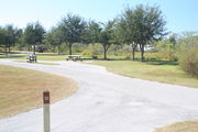 View of campsite #30 from site entry â This is a pull-through campsite, with an asphalt pad for camping units.  On the left of the asphalt pad is the electric hookup and water spigot, surrounded by a protective wooden enclosure.  On the right is a 12â x 20â concrete pad with a picnic table.  Near the concrete pad are a circular ground grill and a pedestal grill.