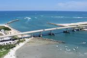 This is a beautiful aerial view of the cove area, cars crossing the bridge over the inlet, north and south jetties and the blue sky and waters of the inlet and Atlantic Ocean.  On the left side of the picture you can see some cars in the parking lot and the bait shop.